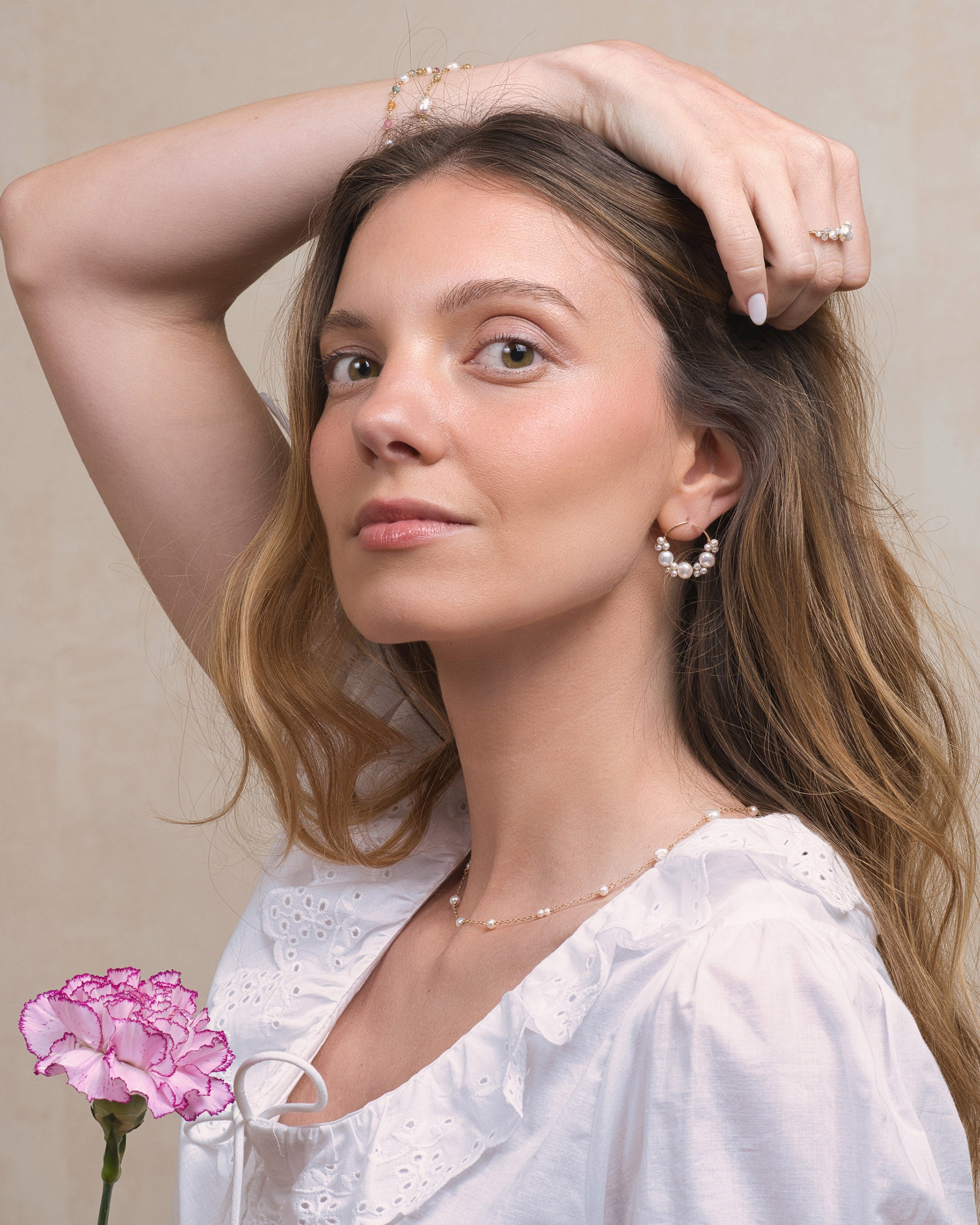 Woman wearing Mamie Coco large baroque pearl cluster earrings and pearl necklace with a pink flower in the foreground