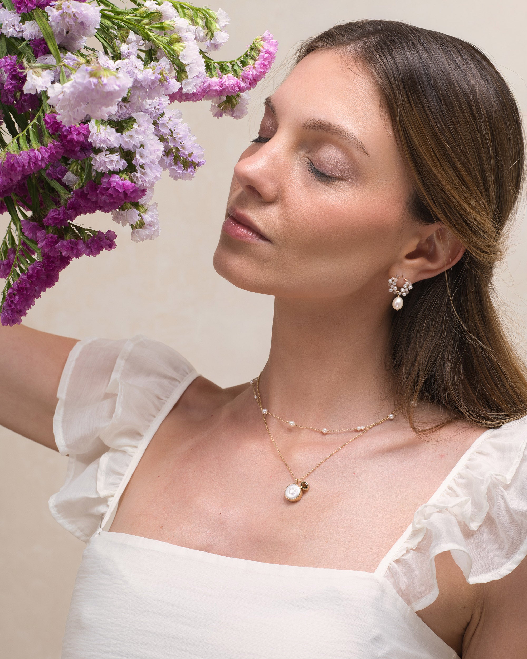Woman with a bouquet of flowers, wearing Mamie Coco bridal pearl earrings, a pearl necklace and a gold bezel pearl pendant with a green tourmaline.
