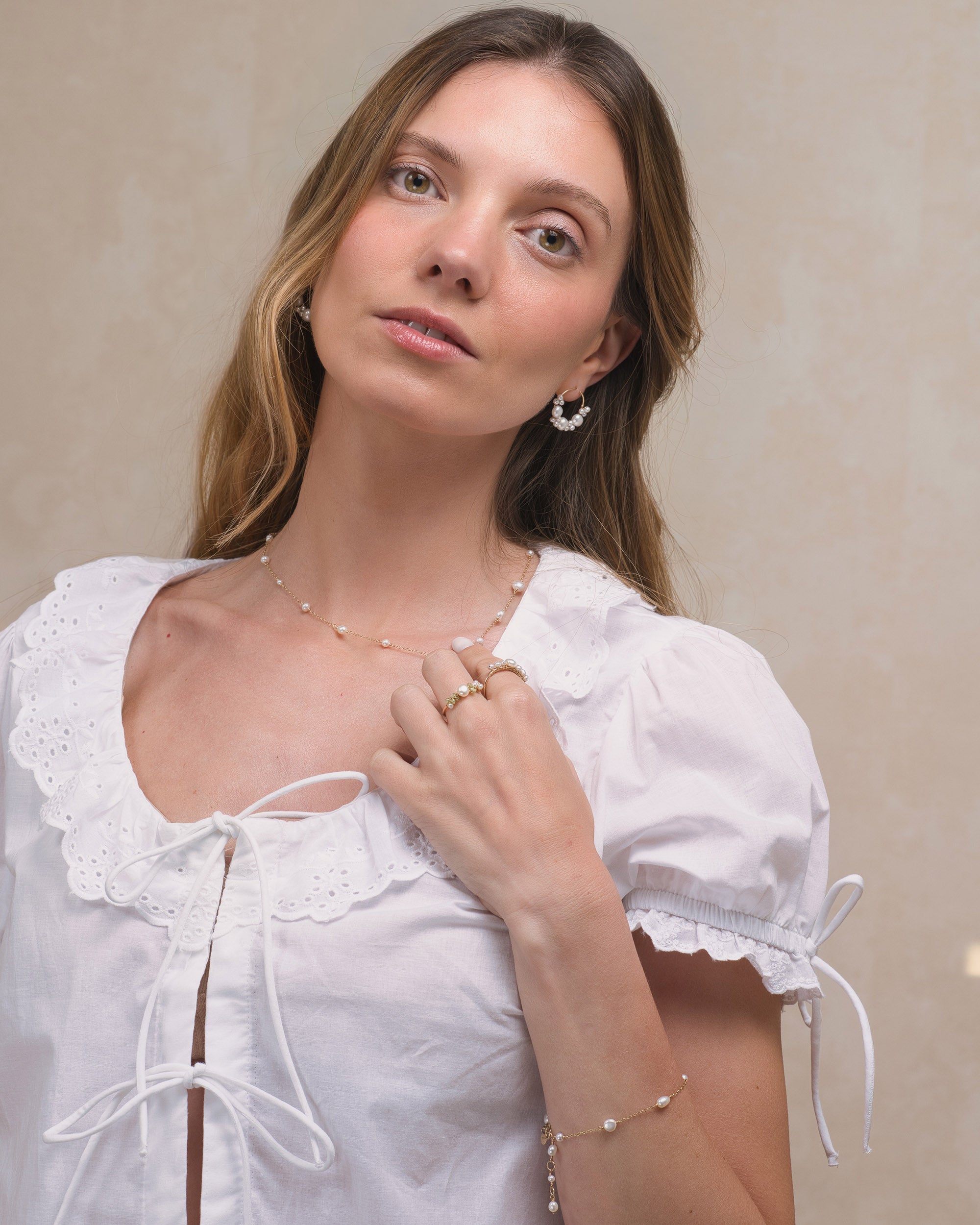 Woman wearing a white lace-trimmed top with Mamie Coco large baroque pearl cluster earrings and pearl necklace against a neutral background